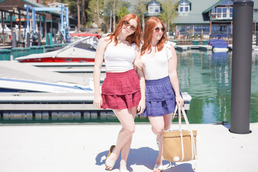 Two girls celebrating the 4th of July in red, white and blue outfits.  Girls are on a boat dock.  Wearing red and blue ruffle skirt.  White tops and Sea Grass beach bag.