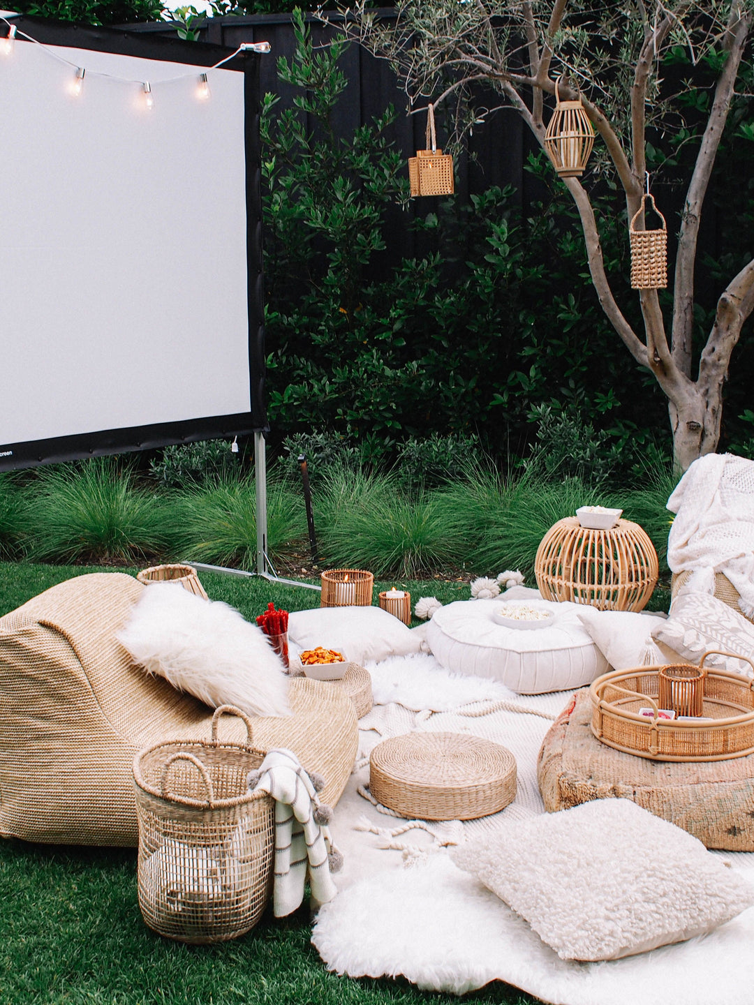 Outdoor movie night setup with comfy chairs, pillows, movie screen and lights