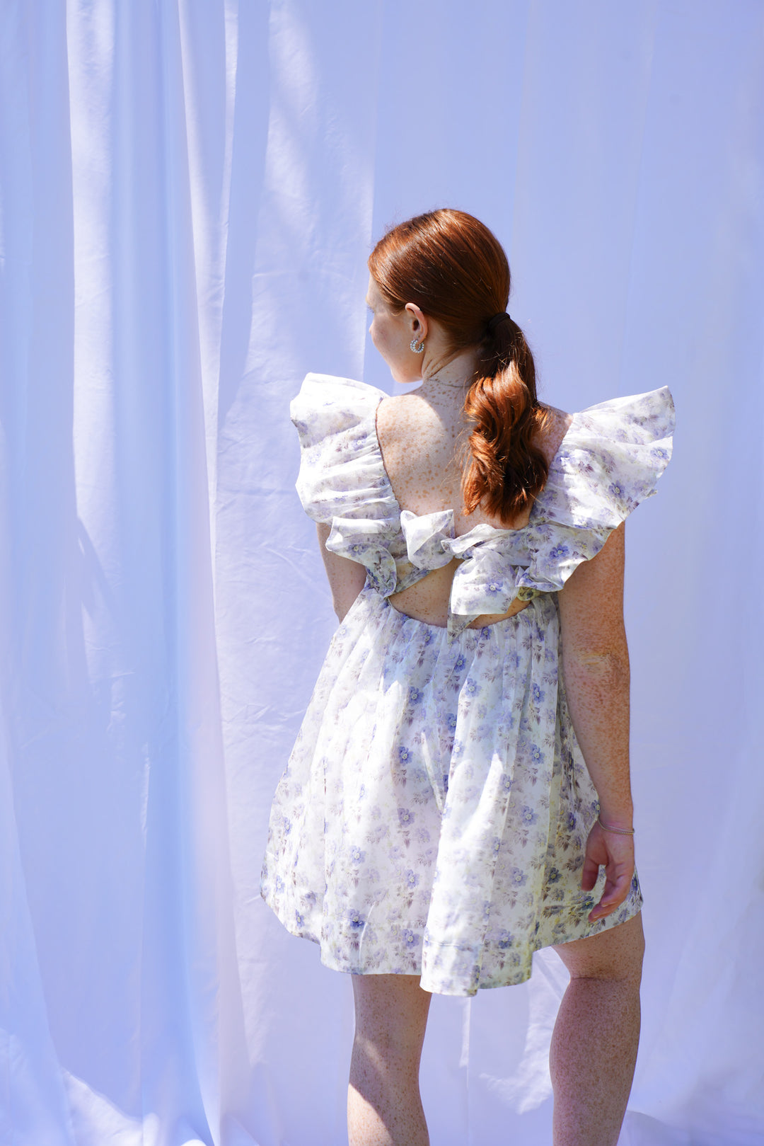 Women wearing blue floral organza dress with ruffle sleeves and bow back