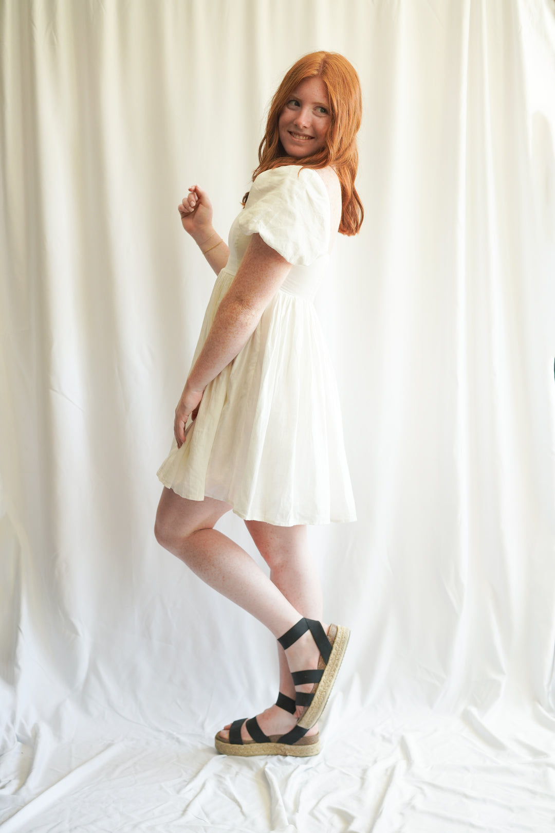 Women wearing white linen babydoll dress. puff sleeves, linen fabric, and smocked back detailing