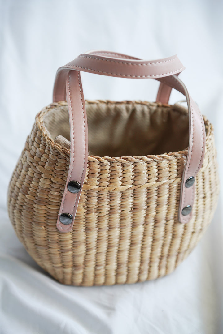 Handbag collection made from pliable sedge seagrass with pink faux leather handles and a convenient drawstring closure