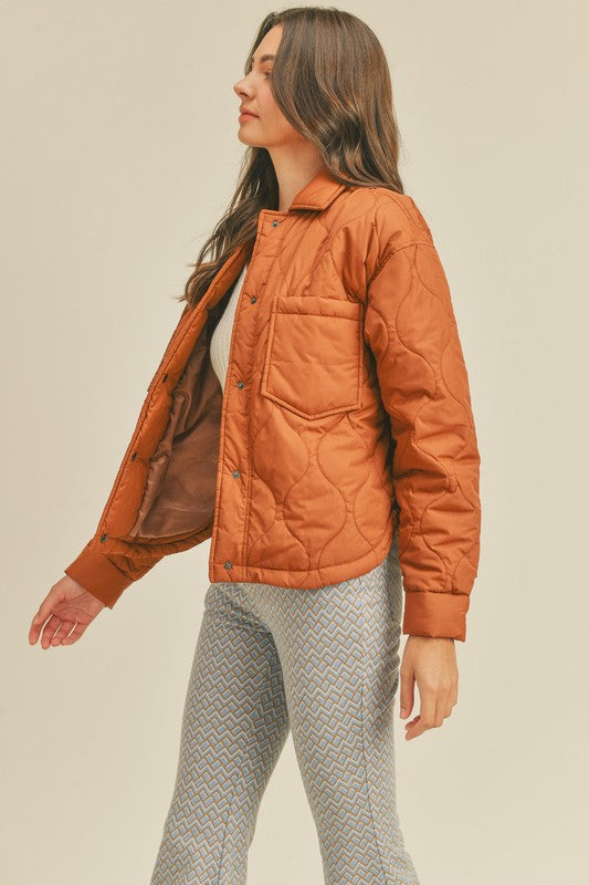 Quilted puffer jacket lined with a collar, front patch pockets, snap button closure, shirttail hem, and snap button cuffs