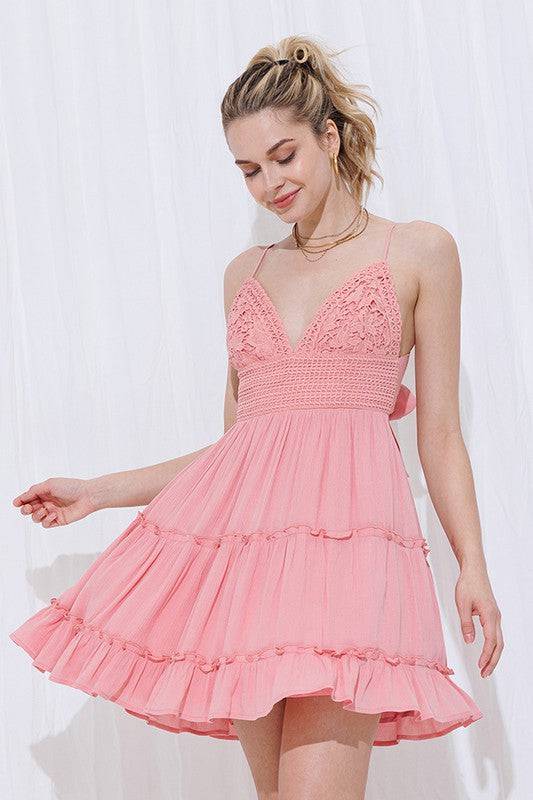 pink color dress with a crochet lace bralette style top with adjustable spaghetti straps and an open back that ties in a bow. The skirt part of the dress is a light material that is tiered for a ruffle look.
